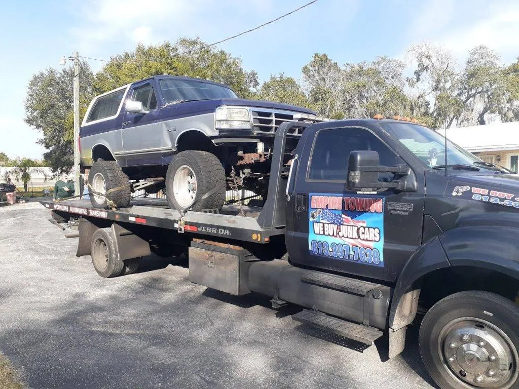 Empire Towing flatbed carrying a blue Ford Bronco on an asphalt driveway